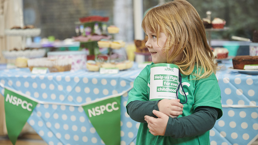 A child smiling while holding an NSPCC collection box.
