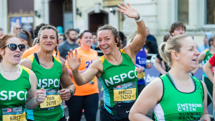 Group of Cardiff Half runners wearing NSPCC vests, one waves with both hands