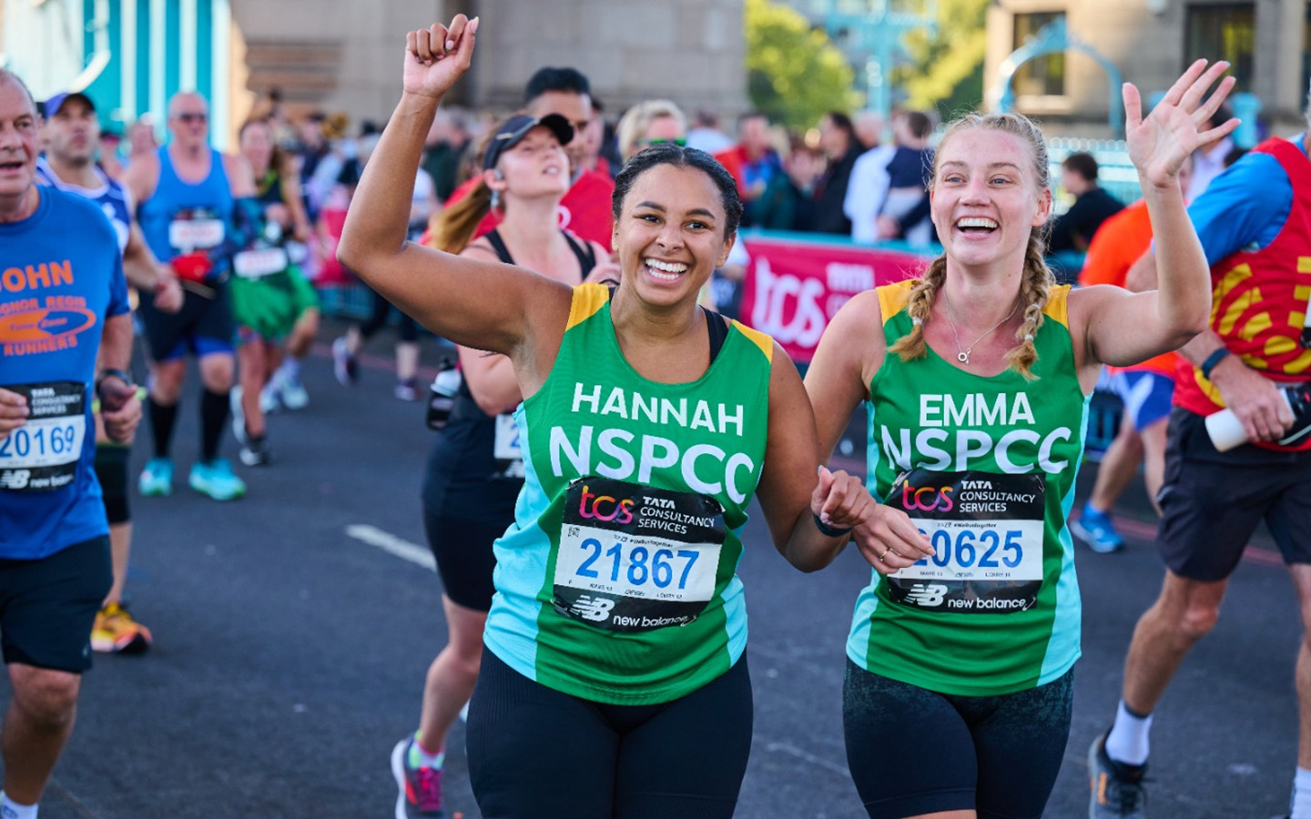 Two women in green NSPCC running vests running and smiling.