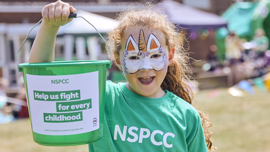 A young girl holds up an NSPCC fundraising bucket
