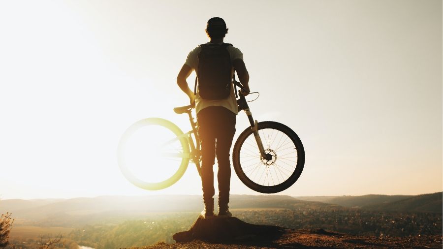 A silhouette of a man at the top of a valley holding an adventure bike