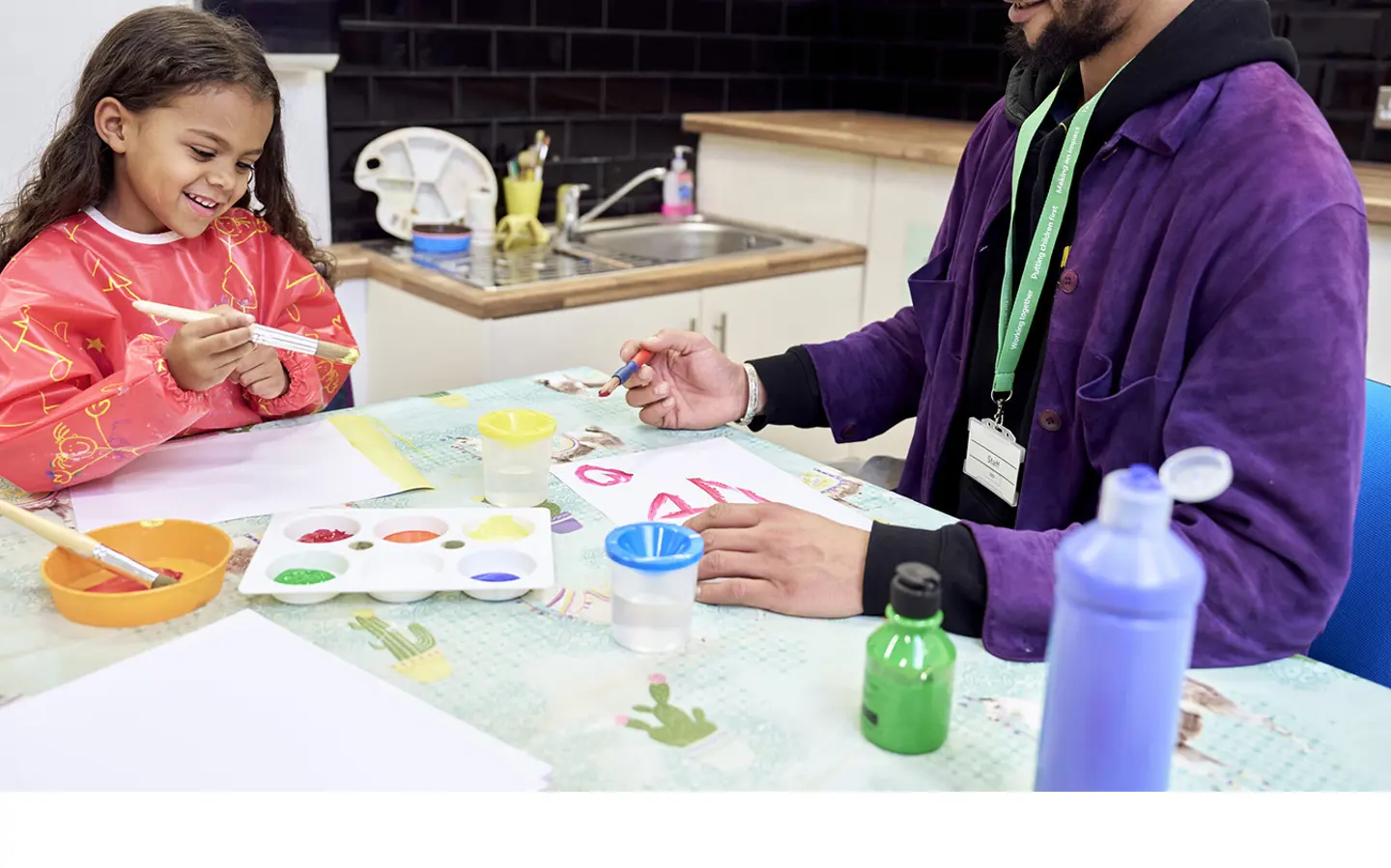 A young child smiling while painting with an NSPCC service practitioner.