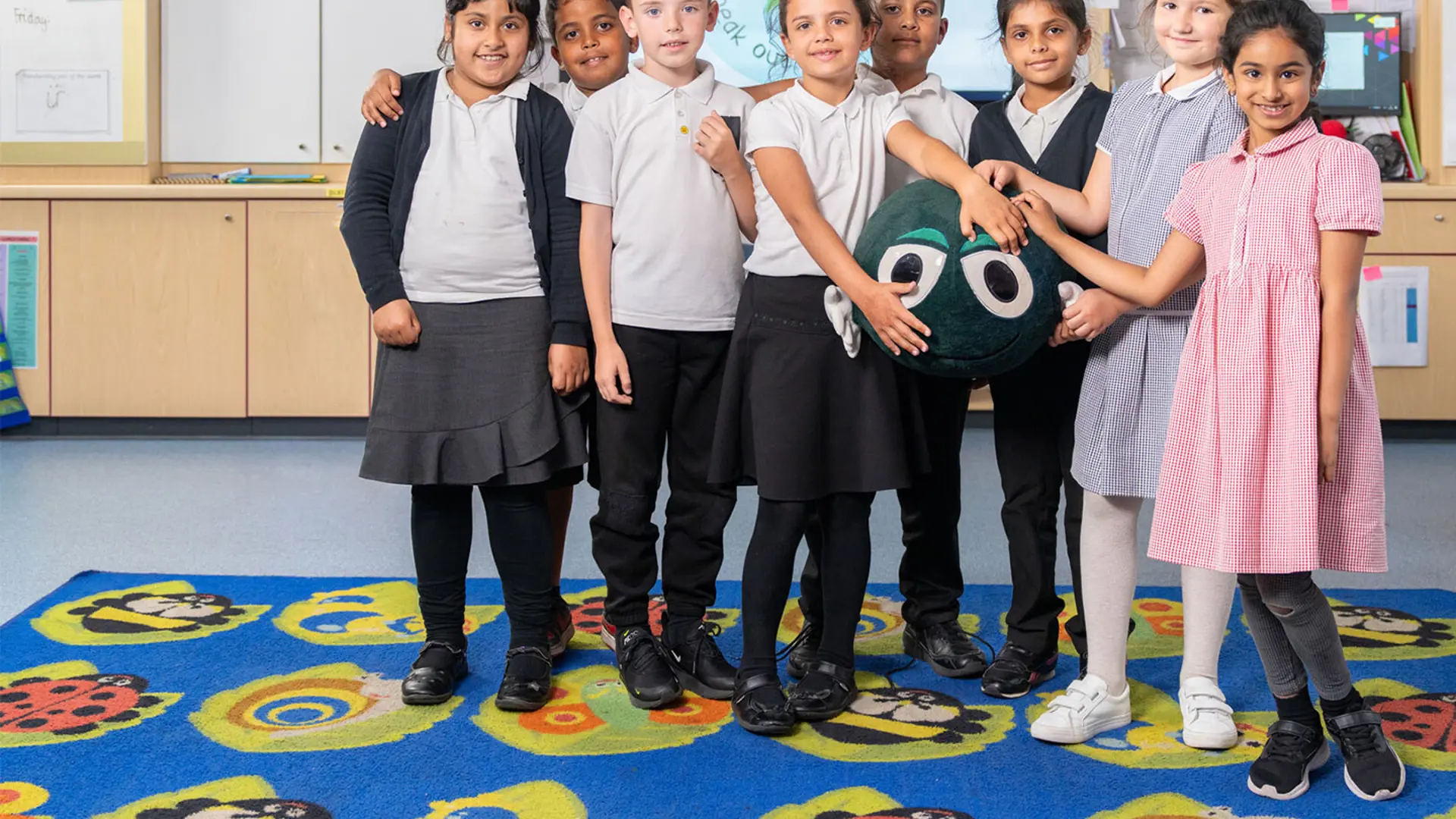 A group of schoolchildren in a classroom holding a toy Buddy