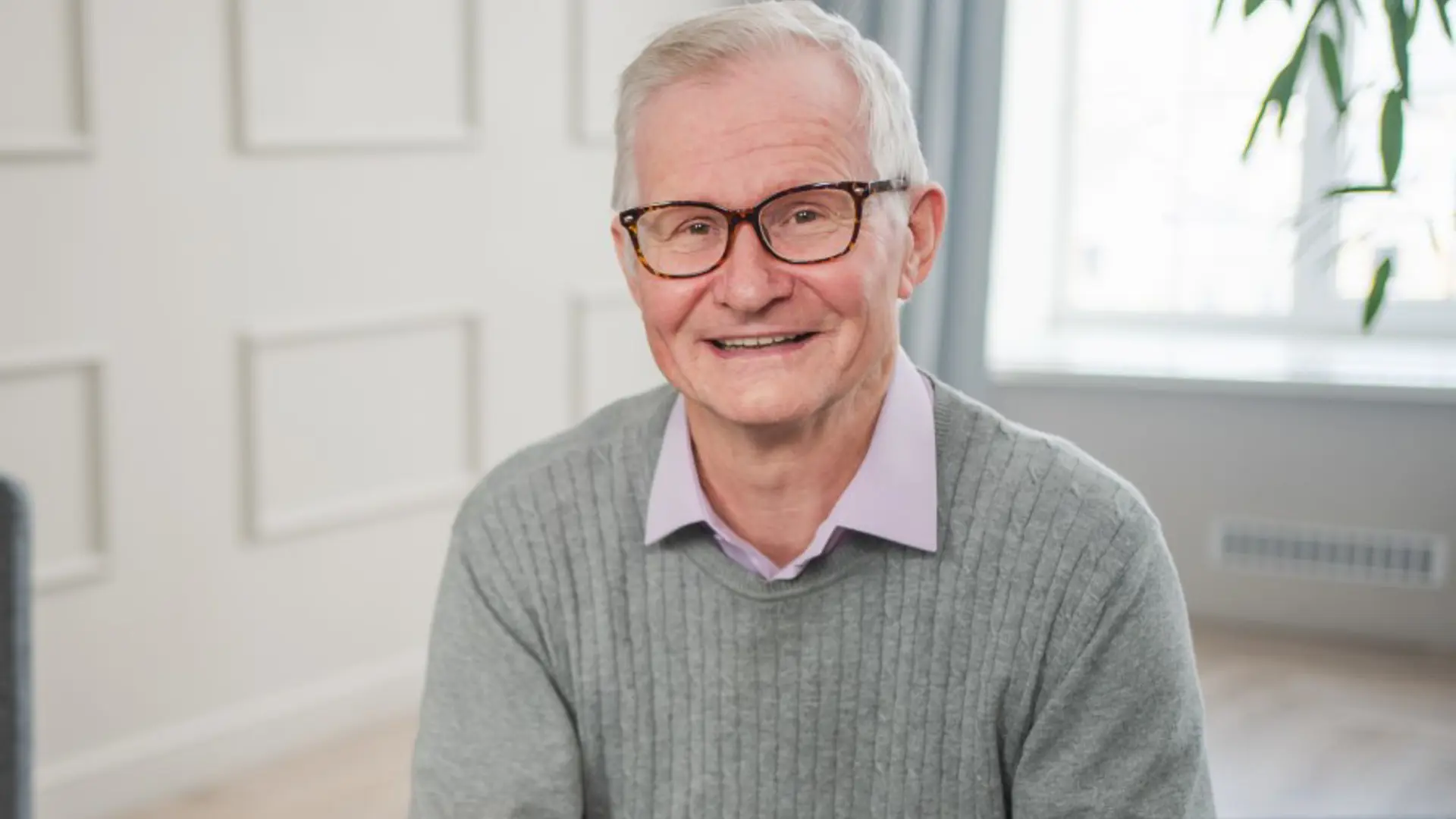 Photograph of a smiling man sat on a sofa.
