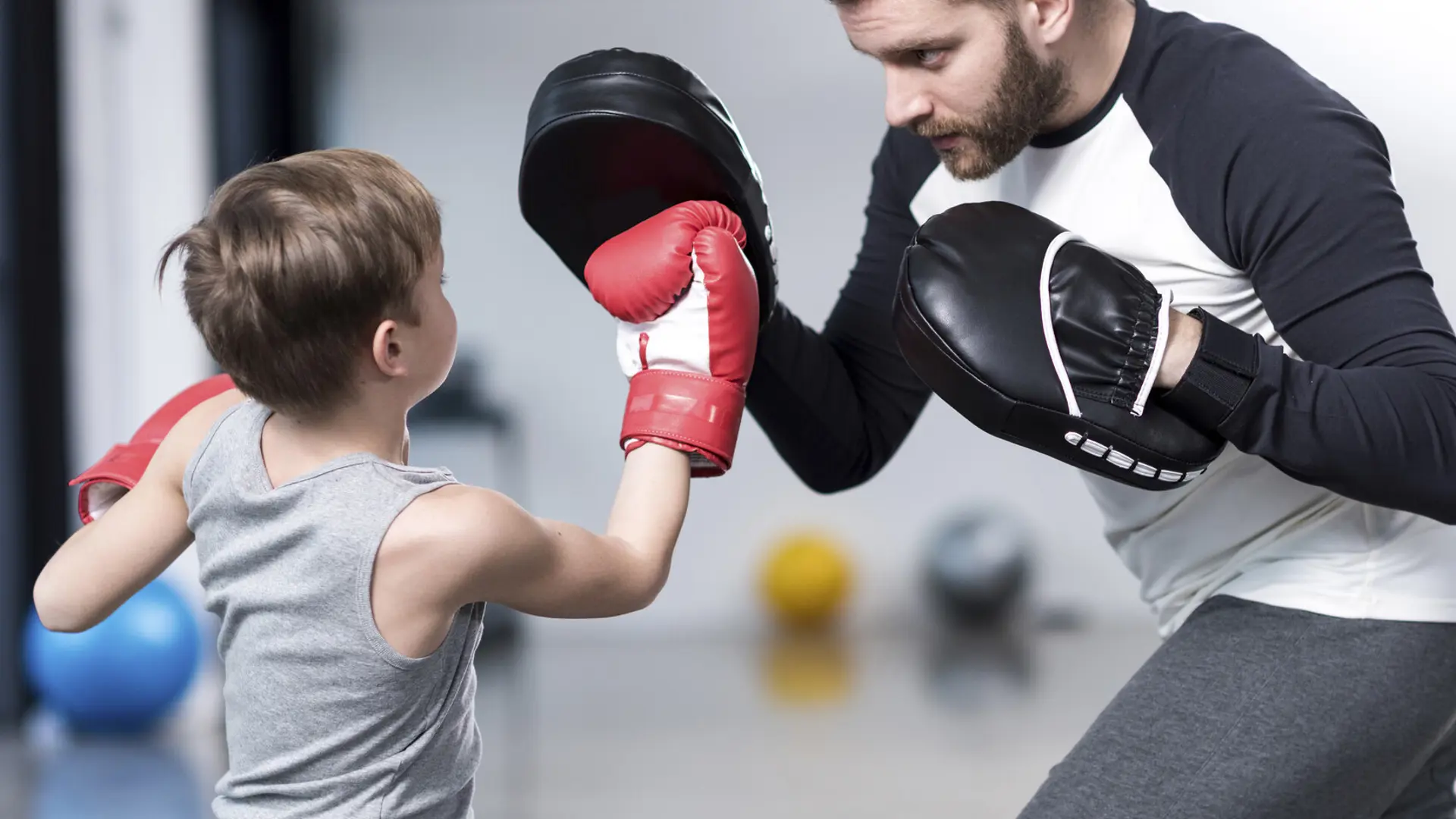 Boy wearing boxing gloves punching man's training mitt