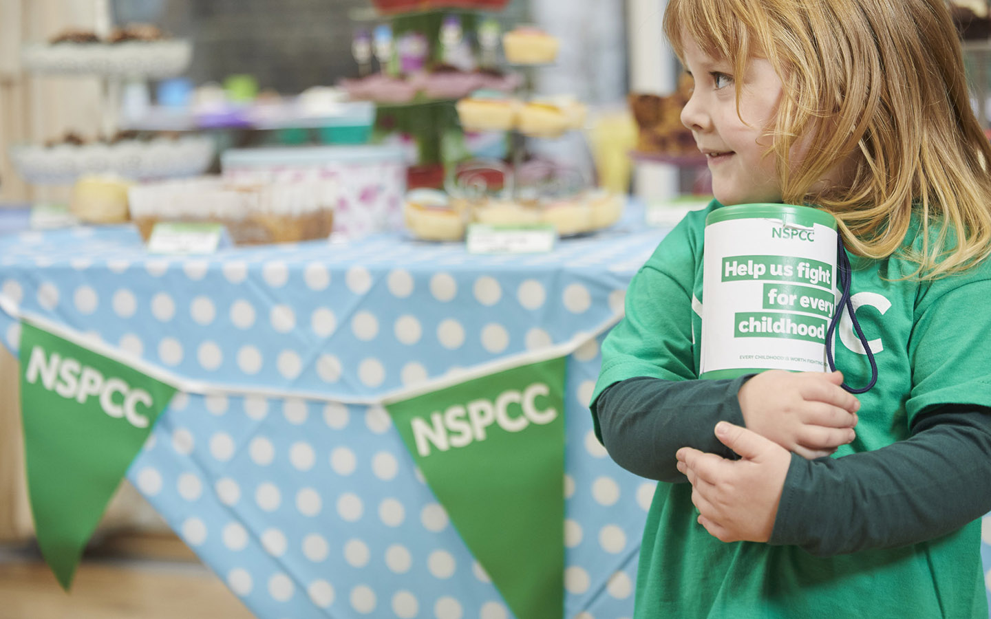 A young girl smiling while holding an NSPCC collection box.