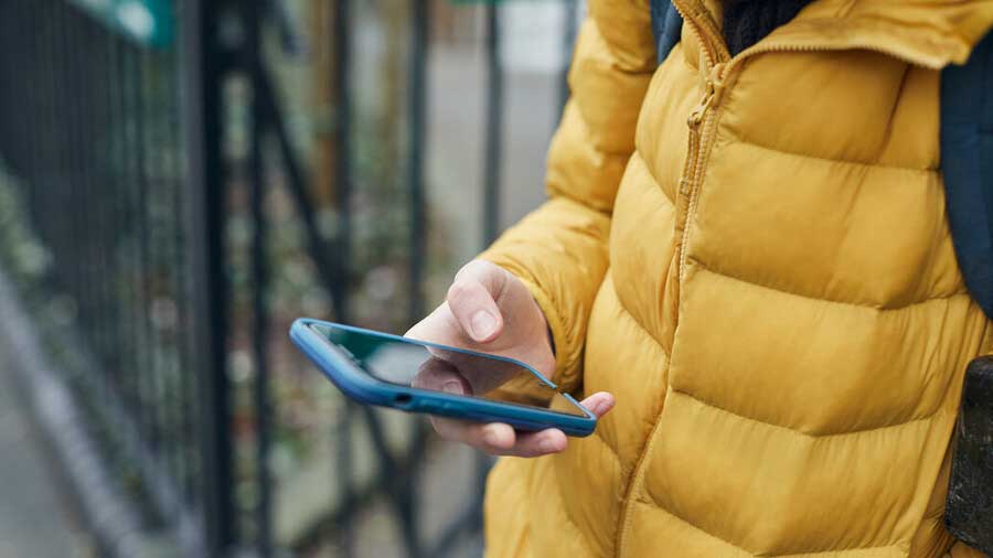 A child wearing a yellow bodywarmer is looking at their phone
