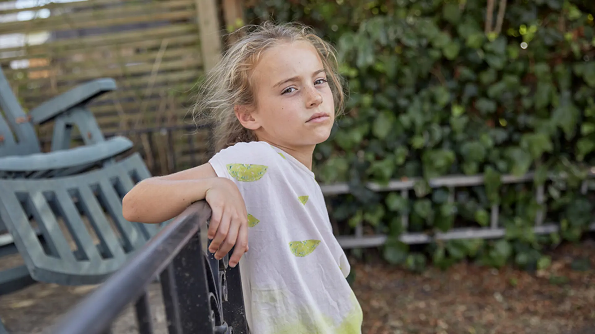 A young child leaning back against railings while staring into the camera.